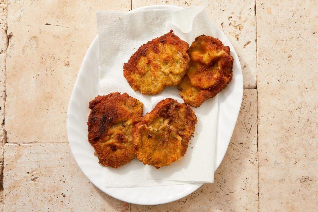 Fried beef milanesa draining on paper towels to remove excess oil