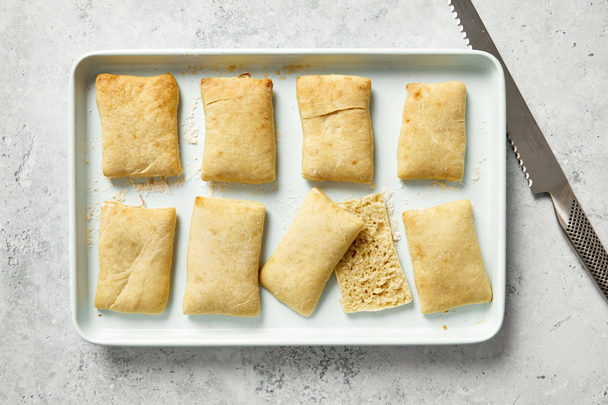 Crispy baked bread sliced open and rubbed with garlic on a baking tray.