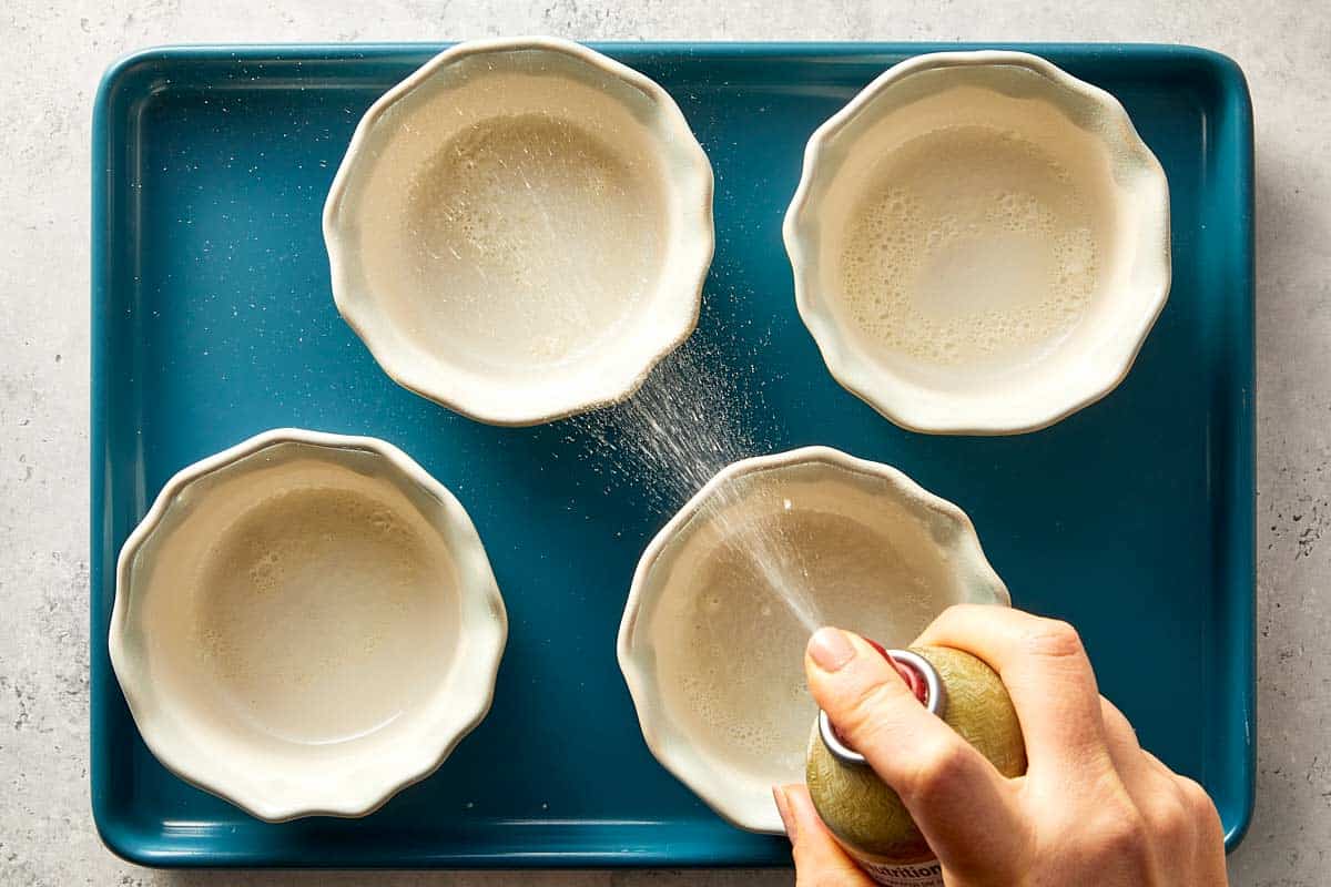 overview of two small bowls being spray with non stick cooking spray.