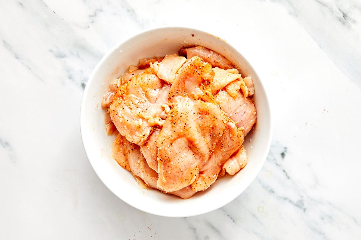 Tossing chicken with spices and oil until evenly coated.
