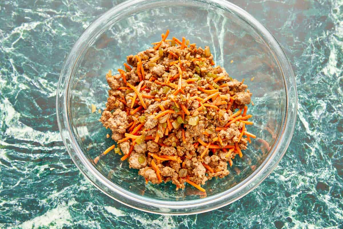 A bowl filled with ground meat and diced carrots, cooling before being used as dumpling filling.