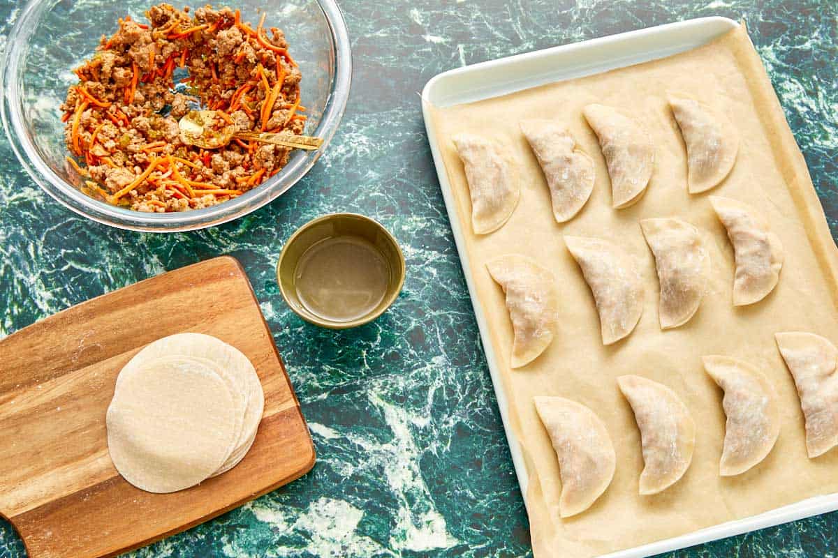 Cutting board with dumpling ingredients, prepared for cooking and ready to be placed on a parchment-lined tray.
