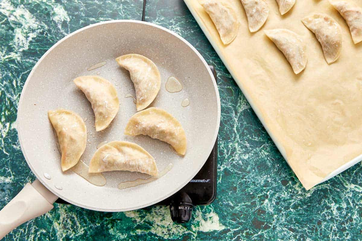 Dumplings frying in a nonstick skillet on a counter, showing golden bottoms and sizzling in oil.
