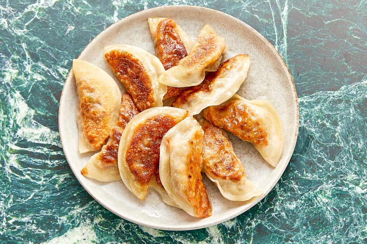 A plate of golden dumplings on a marble table, ready to be served hot with dipping sauce.