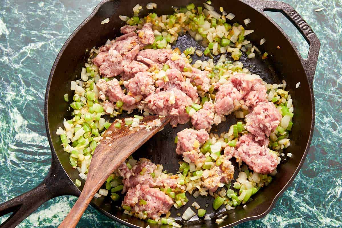 A skillet filled with cooking ground pork and onions, with a spatula mixing the meat until it is browned and cooked through.