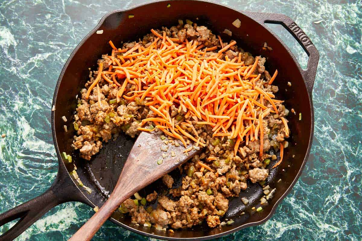 A skillet brimming with sautéed meat and fresh carrots.