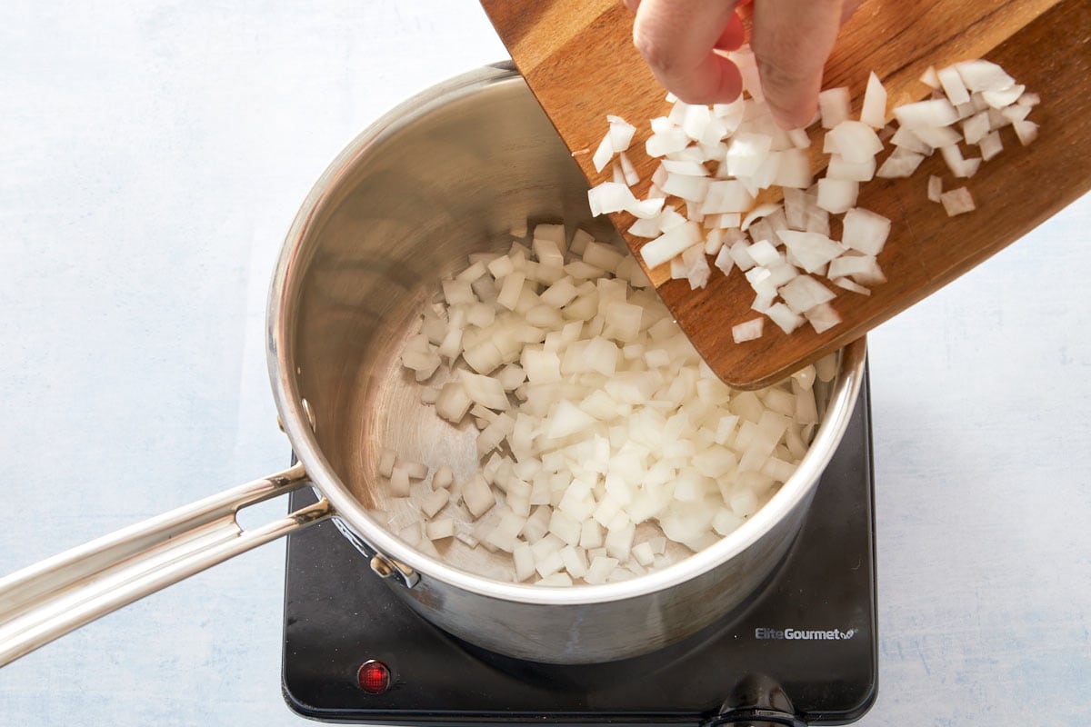 Adding chopped onion to a pot with oil to start the spinach and rice filling.