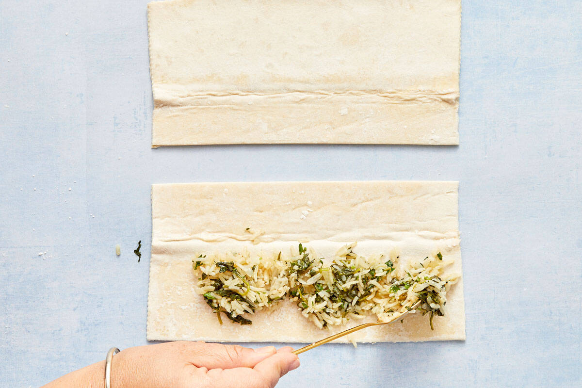 Spooning spinach and rice mixture onto the bottom half of the pastry sheet.