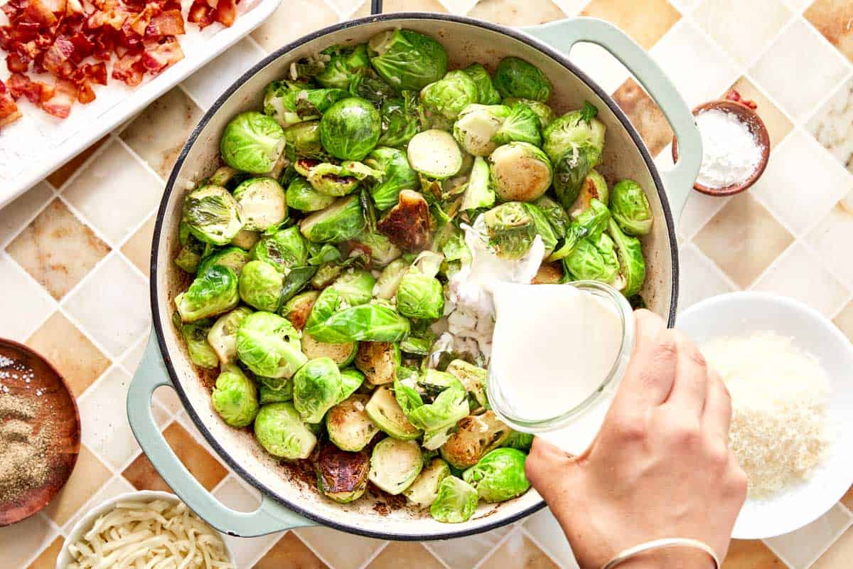 Cream being poured over sautéed Brussels sprouts