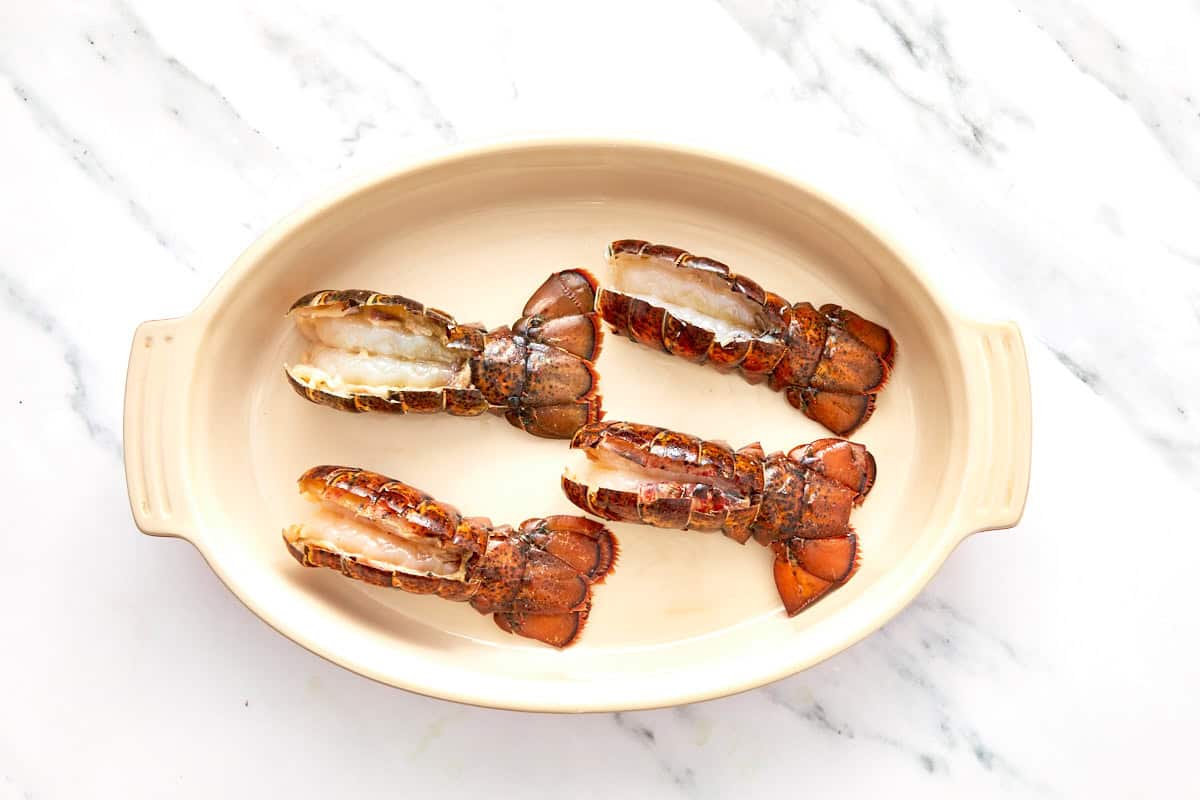Raw lobster tails sliced open and arranged in an oven-safe baking dish, ready for seasoning.