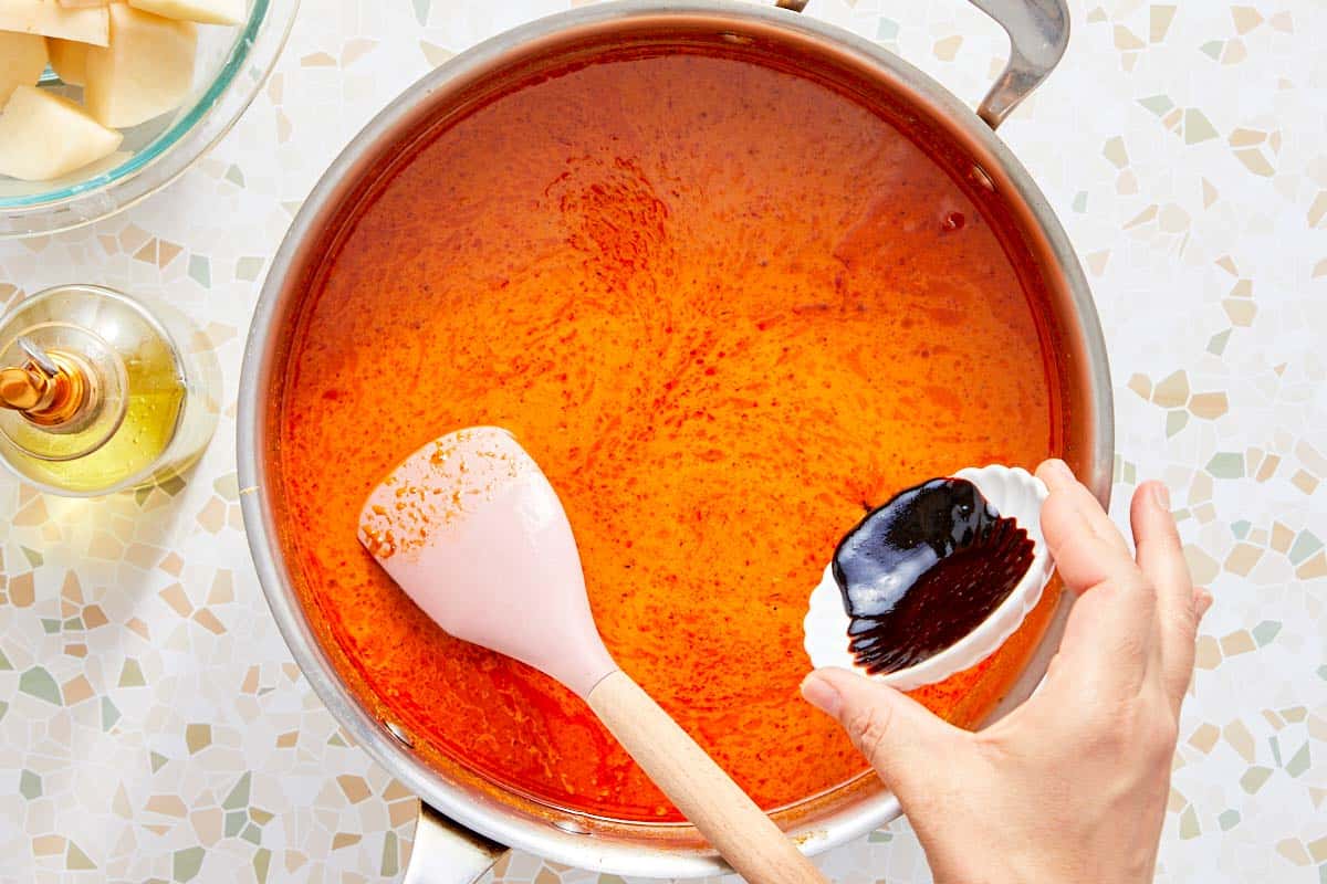 Tamarind paste being added to a pan of red curry sauce.