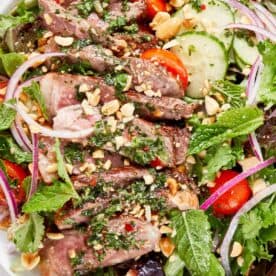 Thai beef salad with sliced seared steak, mixed greens, cucumber, cherry tomatoes, red onion, fresh herbs, and chopped peanuts.
