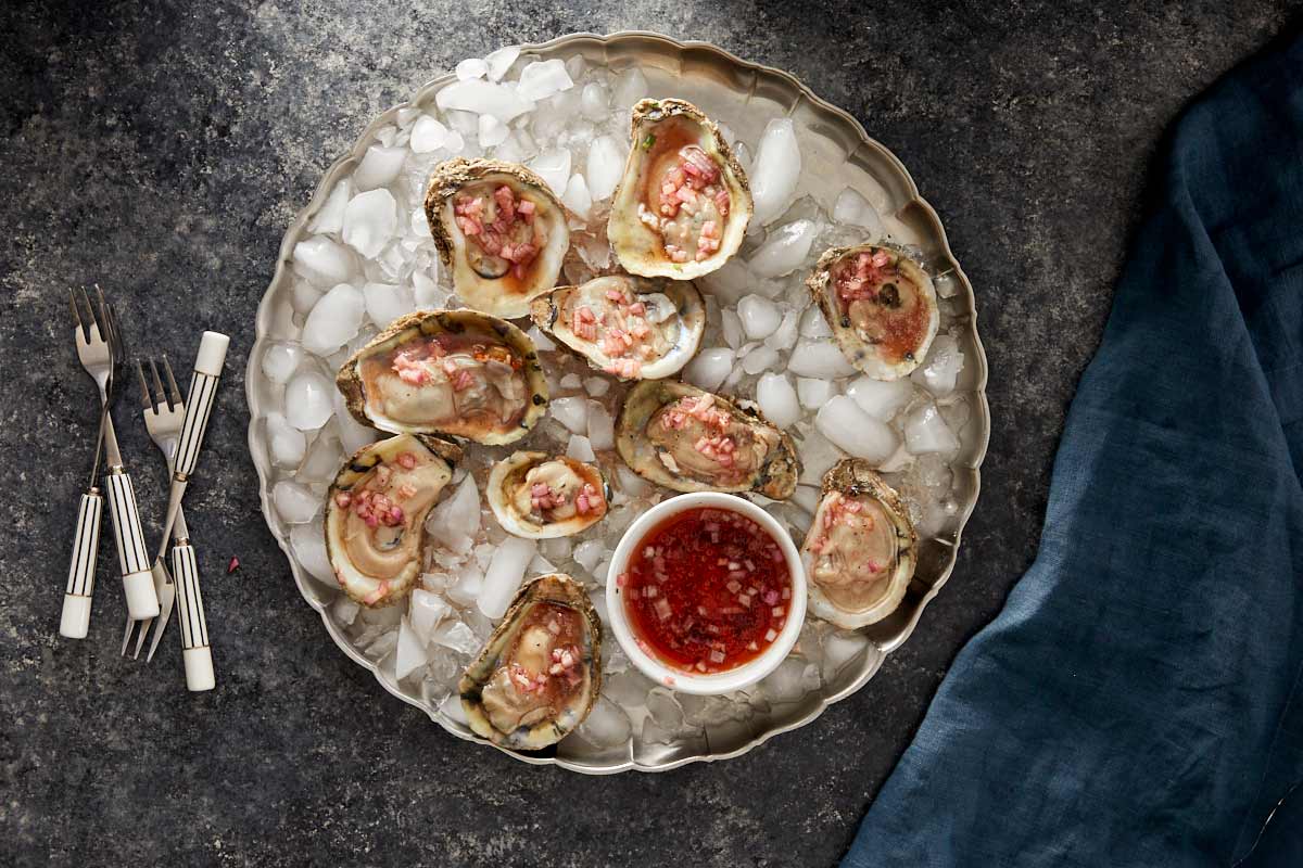 Oysters on ice topped with shallot vinegar mignonette and a small bowl of sauce in the center.