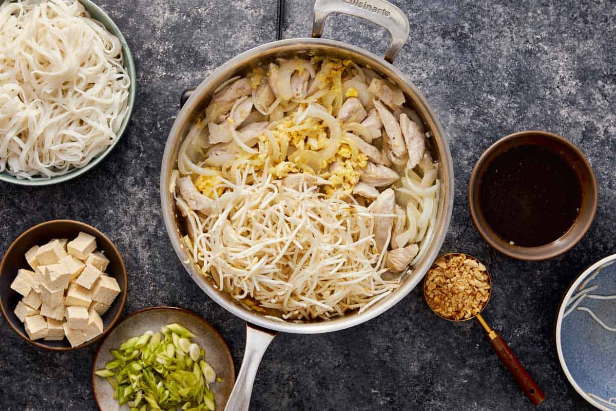 Scrambled eggs cooking on one side of the pan, chicken and onions on the other.