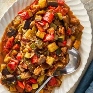 A serving of Ratatouille featuring assorted vegetables, accompanied by a spoon and a glass of red wine.