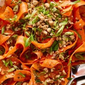 carrot salad with peanuts on top and a spoon on the side
