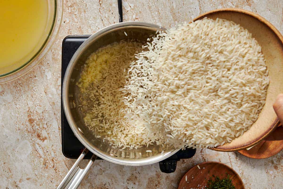 pot on a stove with garlic and butter being saute'd and melted having rice poured in