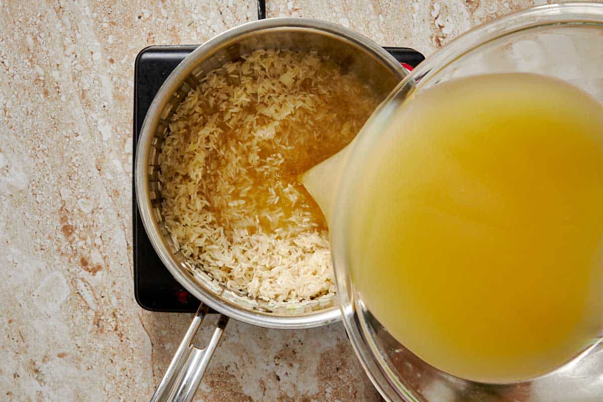 pot on a stove with garlic, butter and rice having stock being poured in