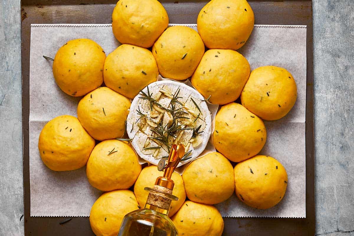 a wheel of camembert on a baking tray with small balls of risen bread dough around it