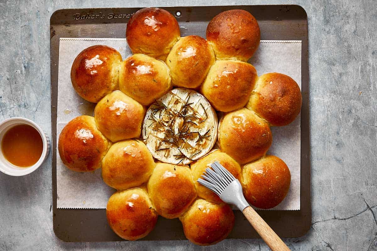 a baked wheel of camembert on a baking tray surrounded by baked bread with hone and salt being sprinkles over