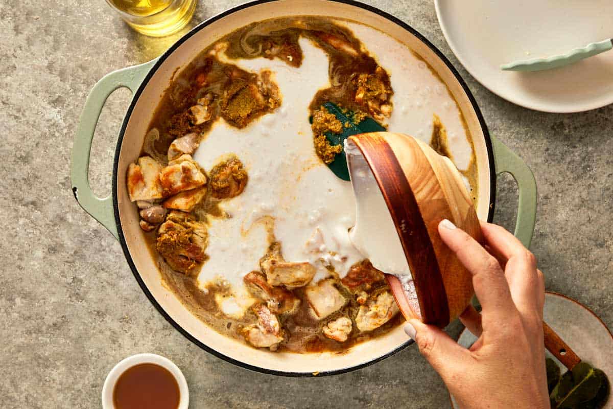 top down shot of a pan with chicken thigh, chicken stock, coconut milk, palm sugar, fish sauce, and kaffir leaves. 