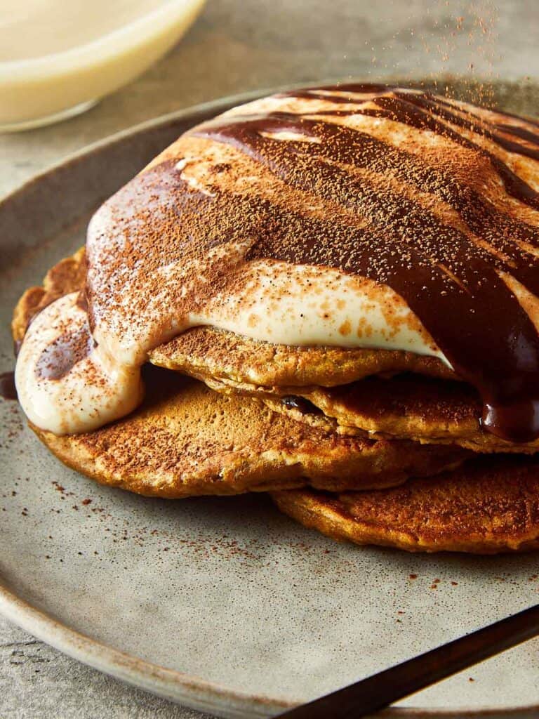 3 pancakes stacked one on top of another, side view, with what looks like greek yogurt on top and drizzling of chocolate coffee on top