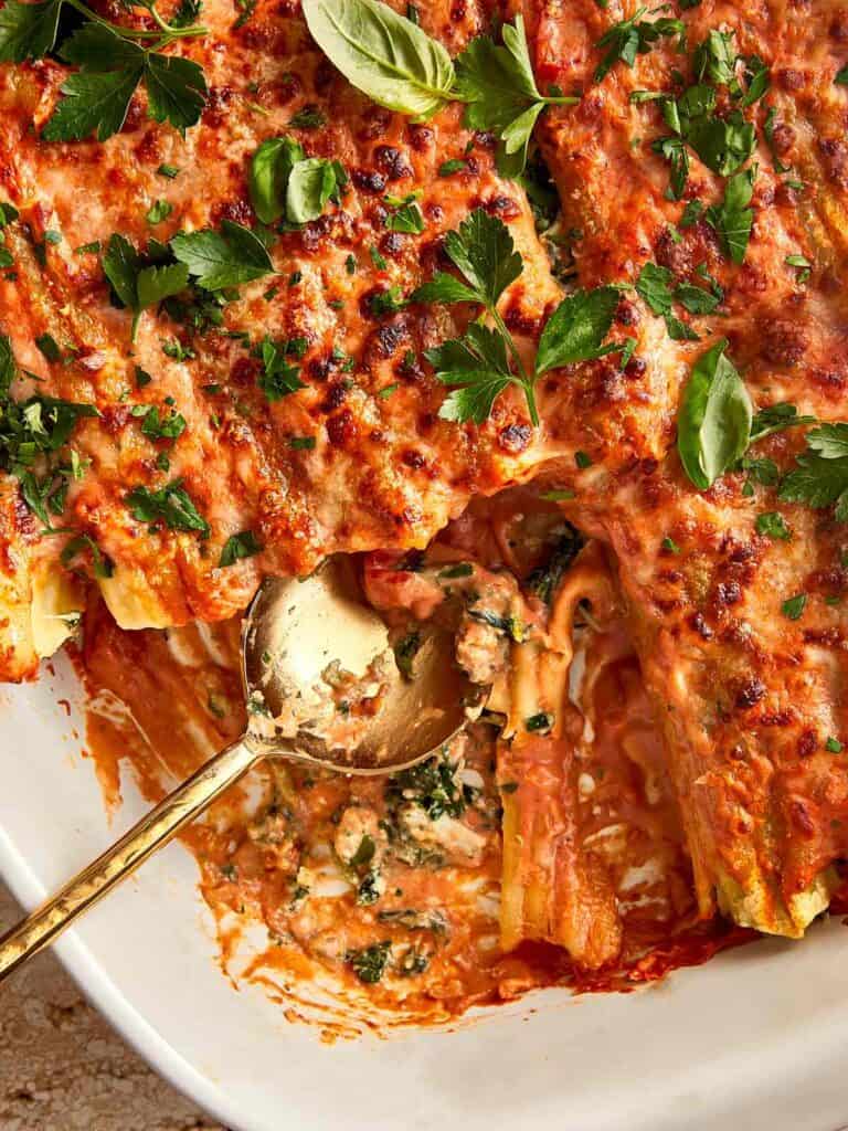 pasta dish top down view of sauce and cheese with green basil on top as decoration a golden spoon is taking some chunks out to show the insides of the pasta tubes are filled with cheese