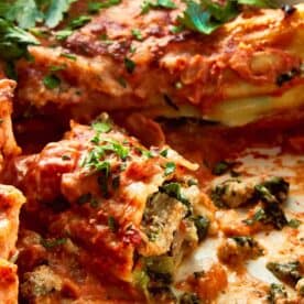 a side view of turkey and spinach cannelloni the tube is cut in half exposing the inside that is green and white and cheese and basil on top