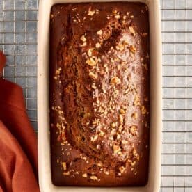 a top down view of banana bread baked in a rectangular loaf pan resting on a wire tray cooling, the banana bread is facing top to bottom