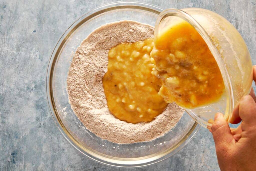 a top down view of a bowl of flour and wet ingredients being poured into the dry ingredients from above the bowl.