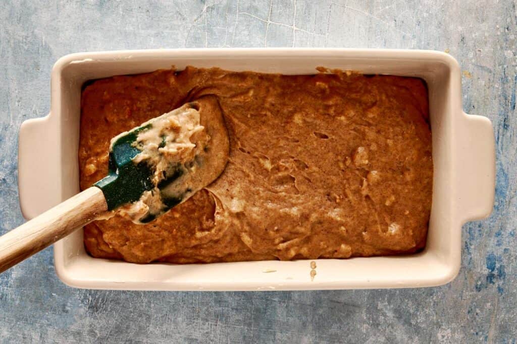 a top down view of a green spatual filling a rectangular loaf pan which is lined with parchment paper