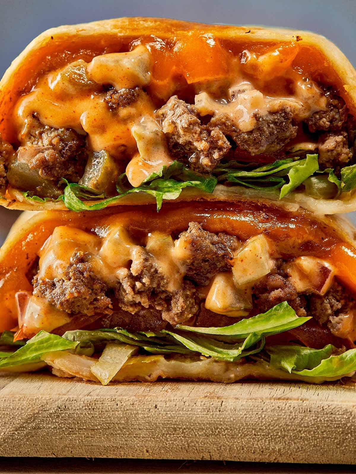 a side view of two halves of cheeseburger wrap with meat melted cheese and sauce close up resting on a chopping board