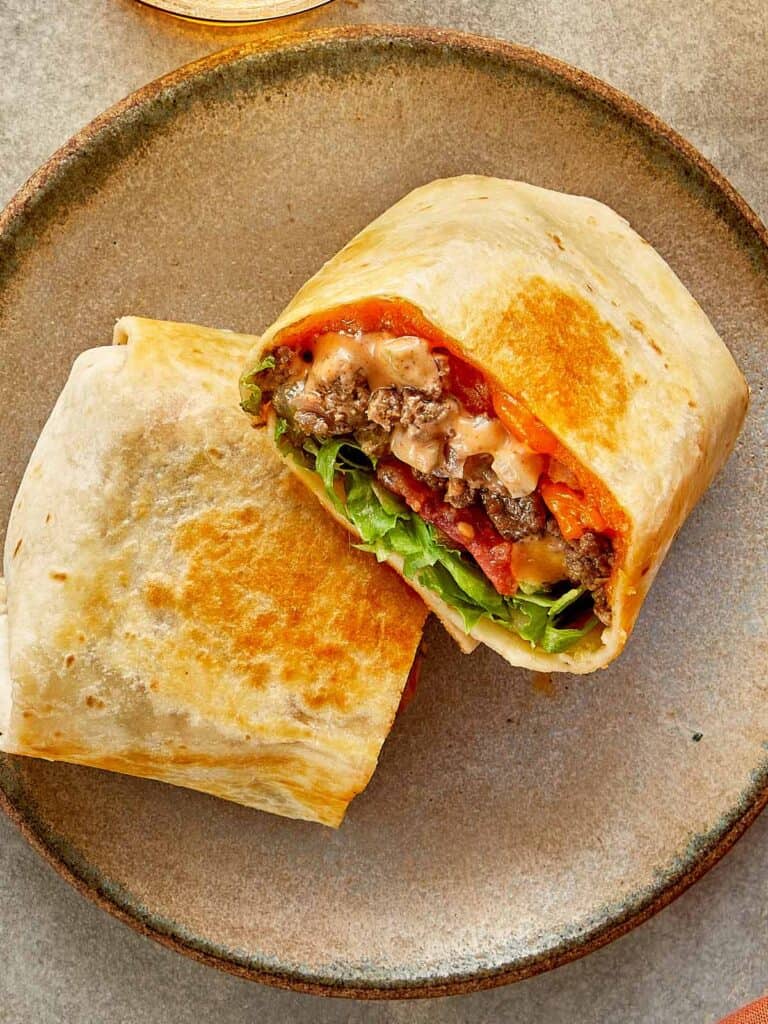 a top down shot of two halves of cheeseburger wrap with meat melted cheese and sauce close up resting on a chopping board