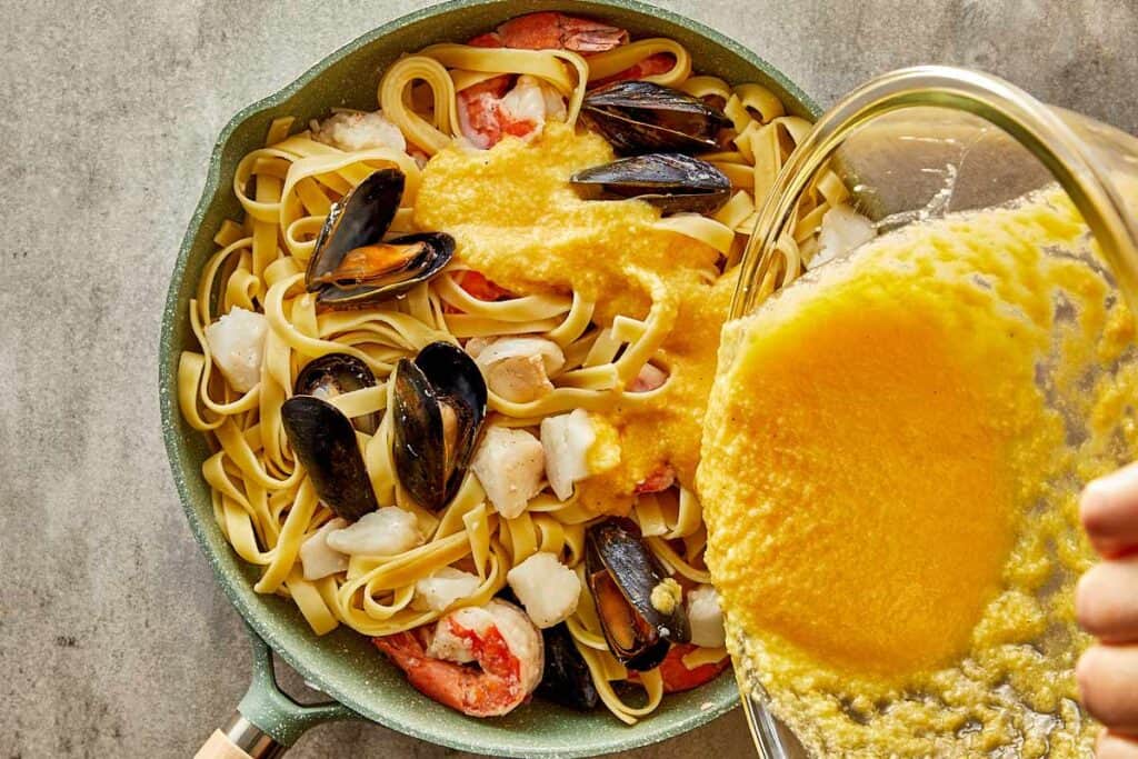 a pan of seafood and pasta and a bowl of liquid egg or yellow being poured into the pan