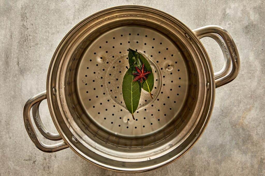 a top down view of a pasta sive with two bay leaves in the bottom of the strainer
