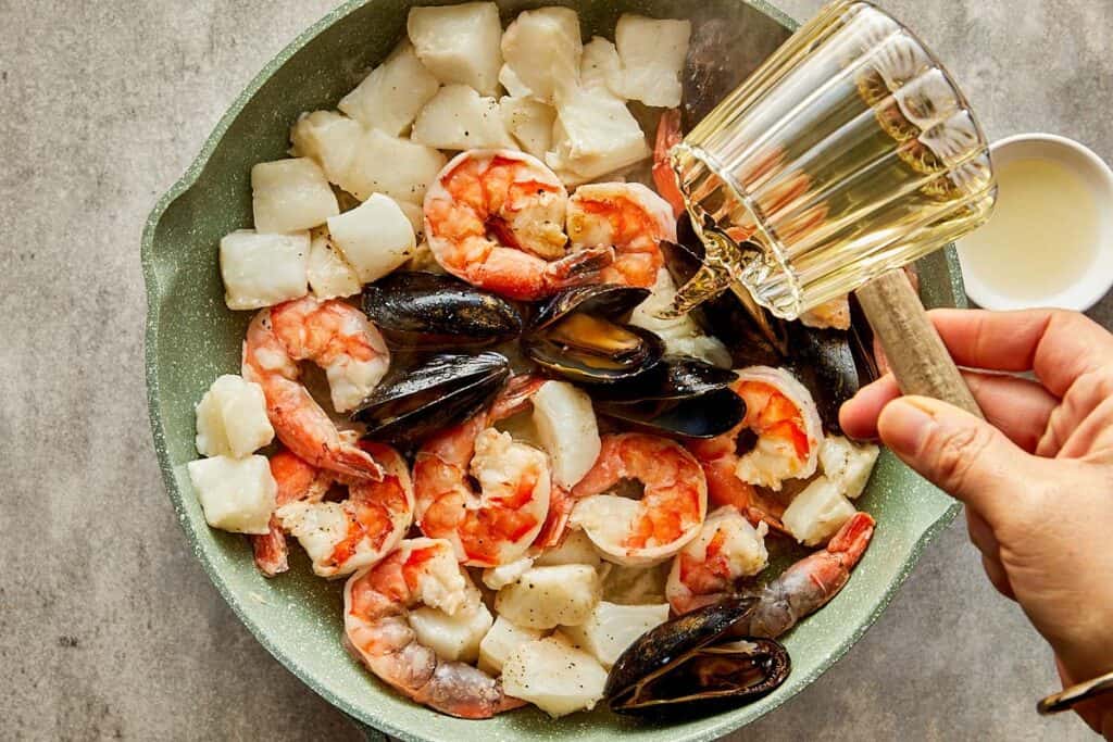 a pan full of seafood being cooked with a jug of water being added to the seafood.