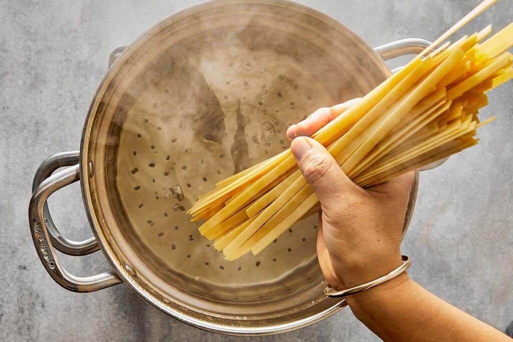 a pasta pot of water boiling away top down view with a hand holding spaghetti uncooked