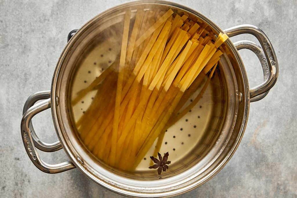 a top down view of a pot of water with pasta being cooked in a pot of water, some of the pasta is out of the water.