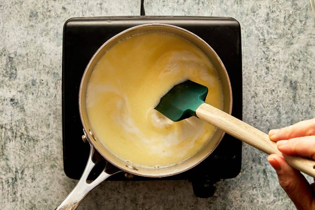 a top down view of a pan of milk and a mixing rubber spoon mixing in the pot