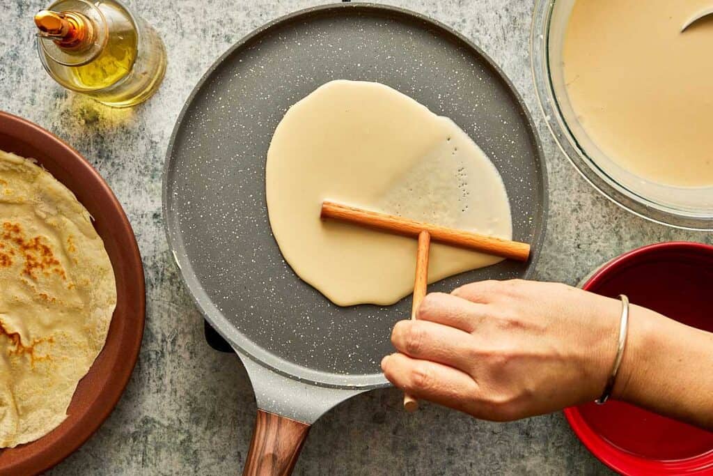 a top down view of a crepe being made using a crepe tool to flatten the batter on top of a crepe pan