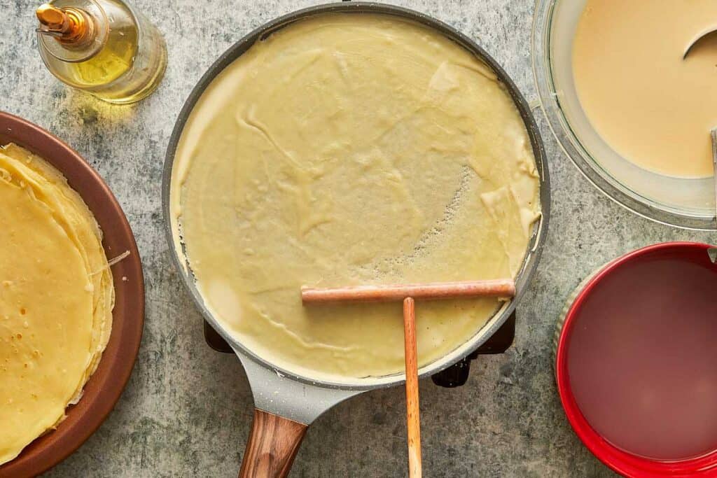 a top down view of a crepe being made using a crepe tool to flatten in on top of a crepe pan