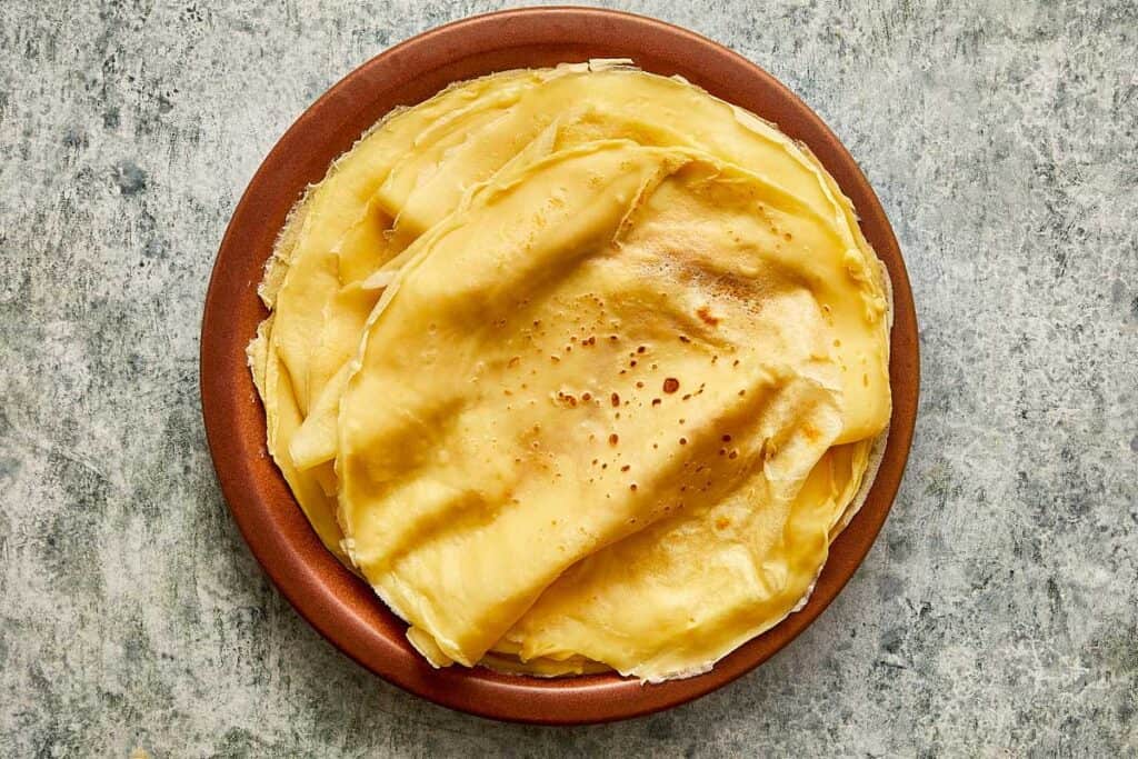 a cooked crepe sitting on top of a ceramic brown plate, the crepe is creased as it sits on the plate
