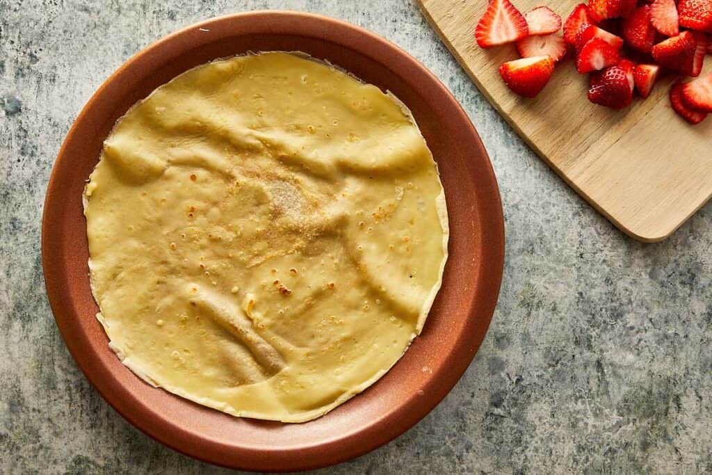 a cooked crepe sitting on top of a ceramic brown plate, the crepe is creased as it sits on the plate