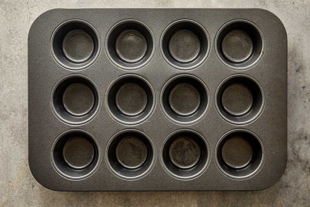 A top down view of a muffin tray non stick dark grey with 12 holes
