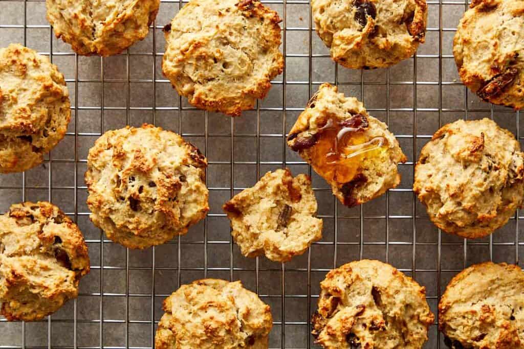 a collection of muffins sitting spaced out on a wire rack cooling with the middle one cut open to show the insides