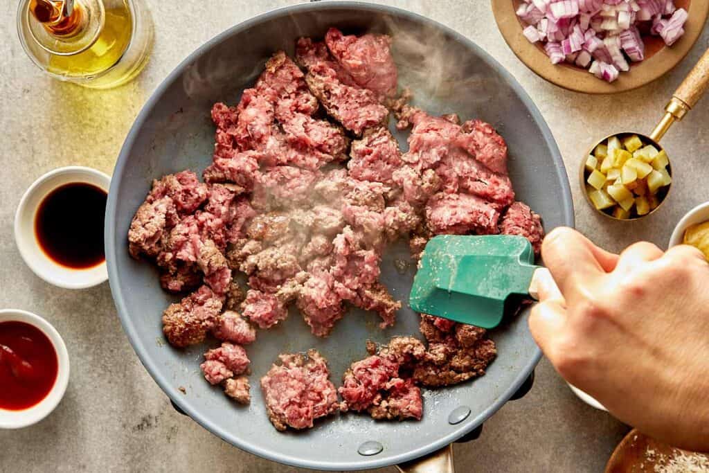 a top down view of a frying pan with mince meat inside being stirred with a spatula