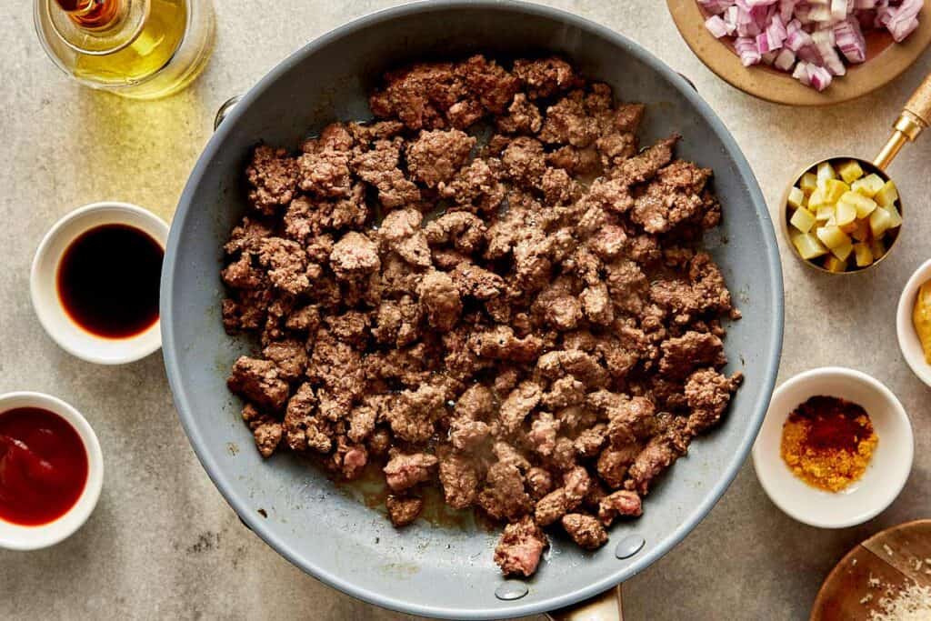 a top down view of a pan filled with mince meat being cooked on a benchtop stove, the meat is browning up