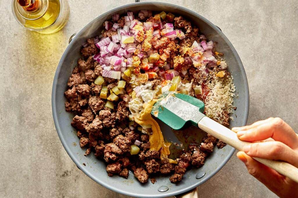 a top down view of a pan filled with mince meat being cooked on a benchtop stove, there is onions and garlic inside now