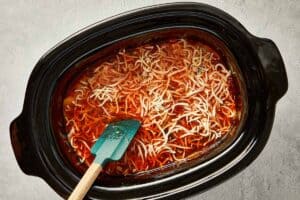 Shredded mozzarella added to hot lasagna soup in a slow cooker, beginning to melt into the sauce