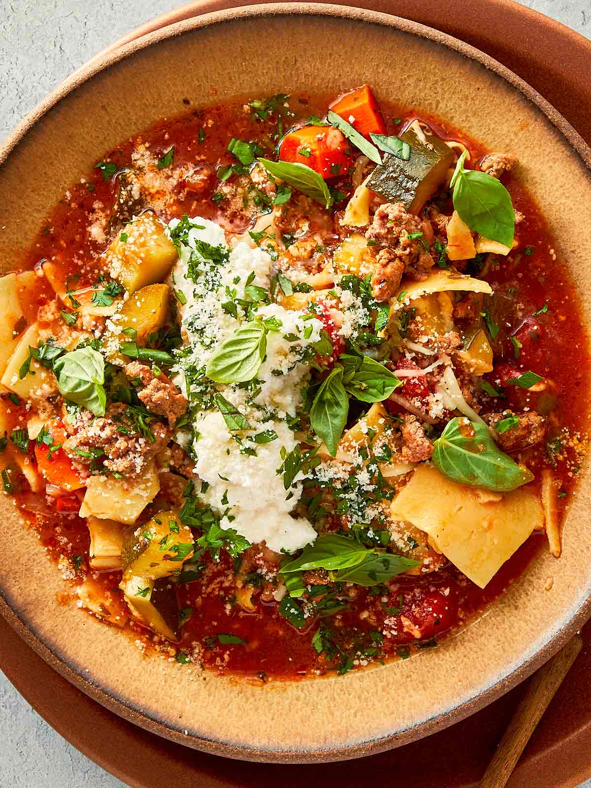 close up of lasagna soup served with ricotta and parmesan cheese and topped with basil and parsely.